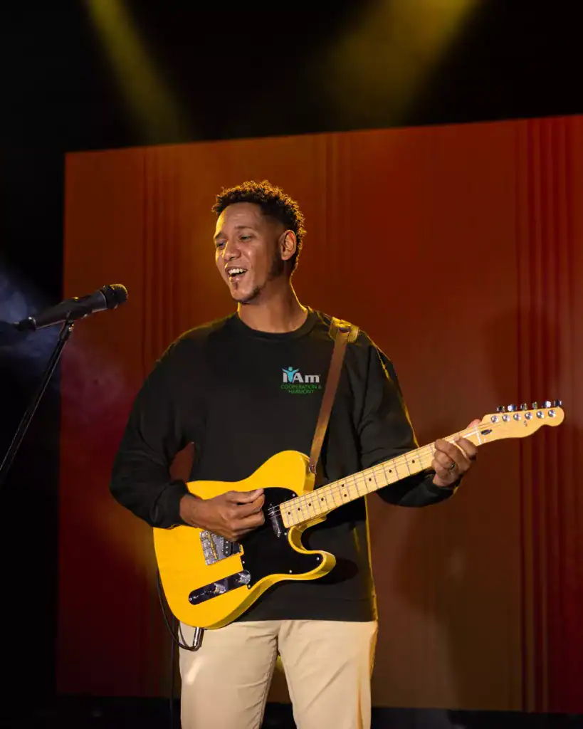 Young man playing electric guitar on stage at marketplace event.