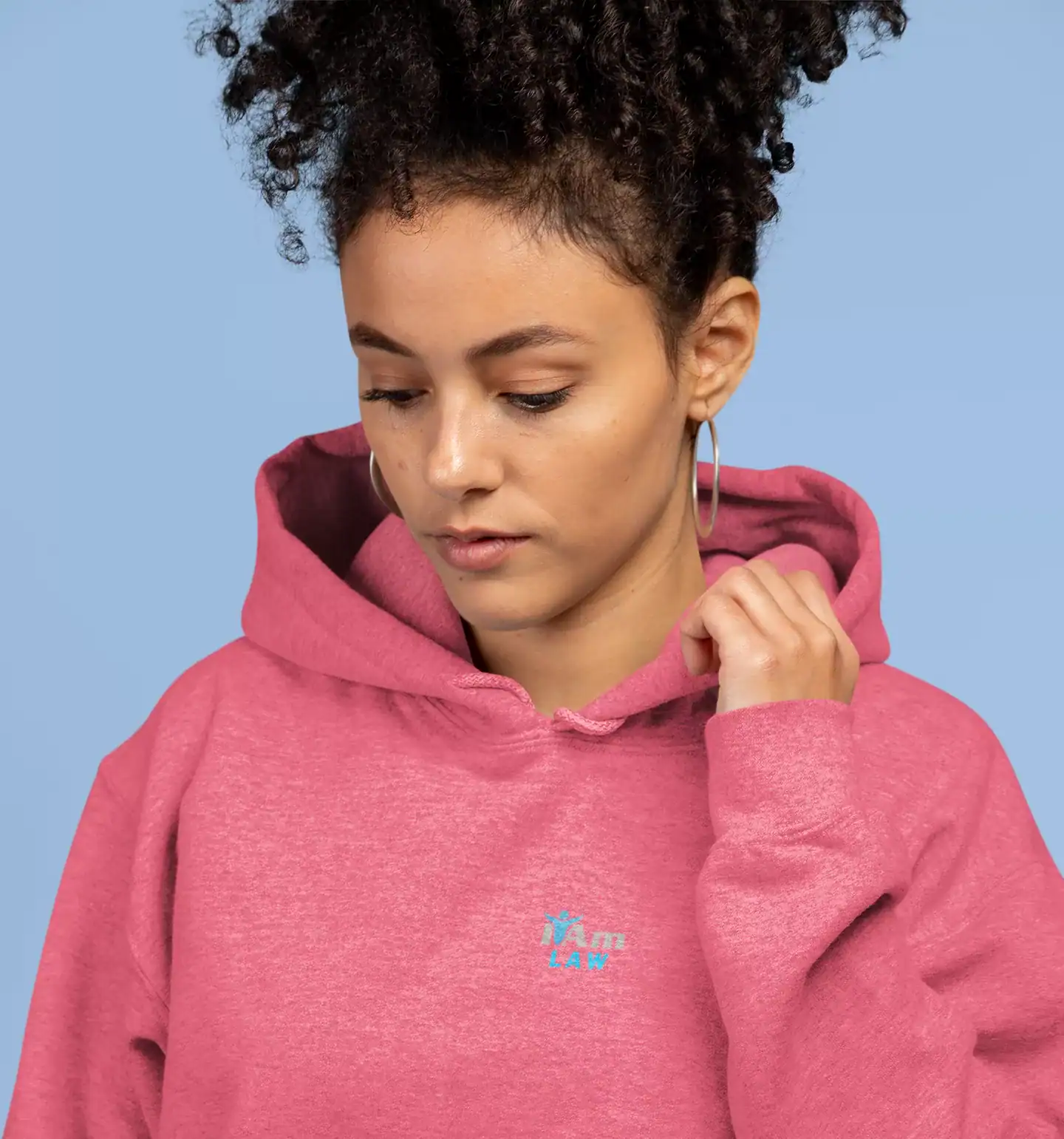 Young woman in pink embroidered hoodie with 'I Am Law' logo, looking down.