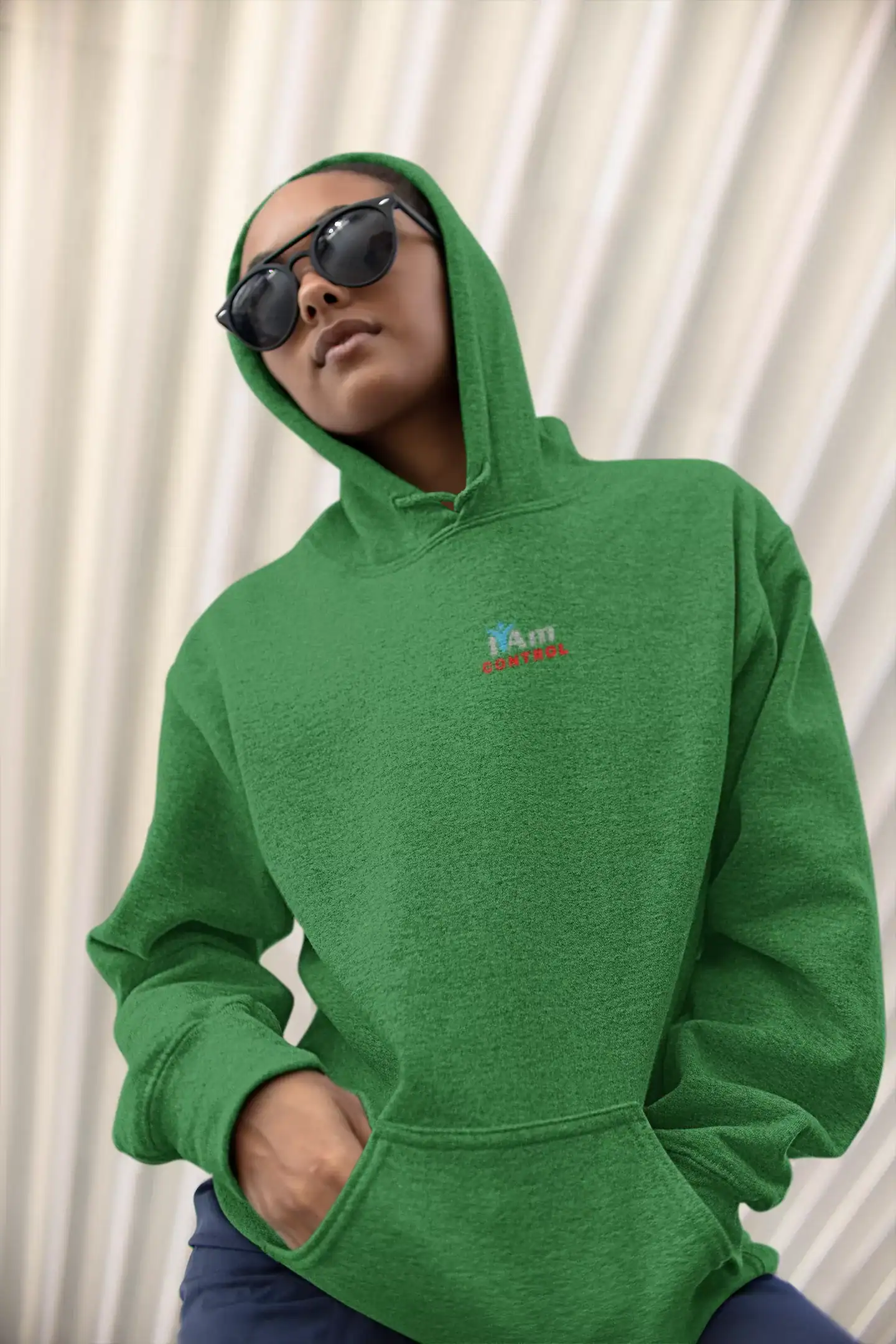 Woman in green hoodie and sunglasses posing confidently indoors.