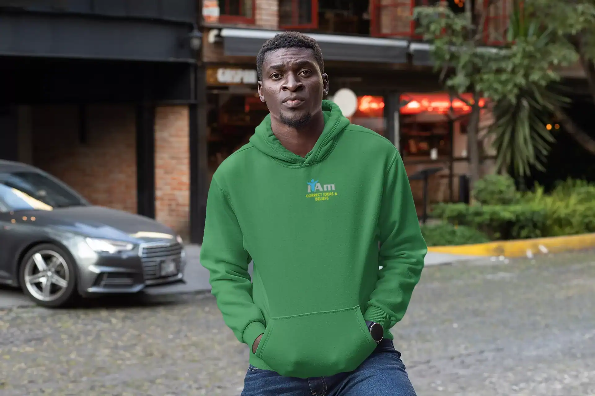 Young man in green hoodie standing outdoors in urban setting.