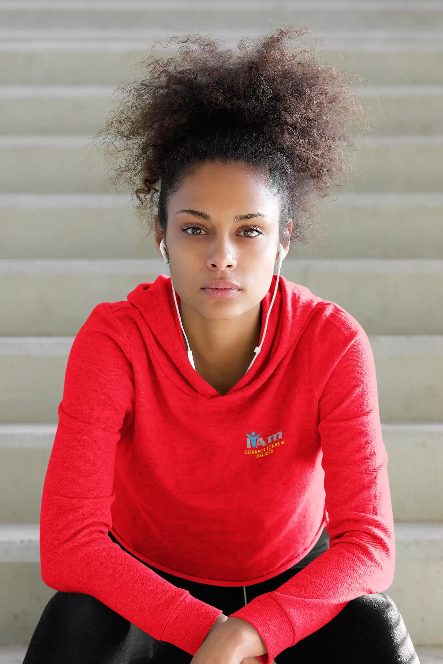 Young woman in red hoodie sitting on stairs with earphones.