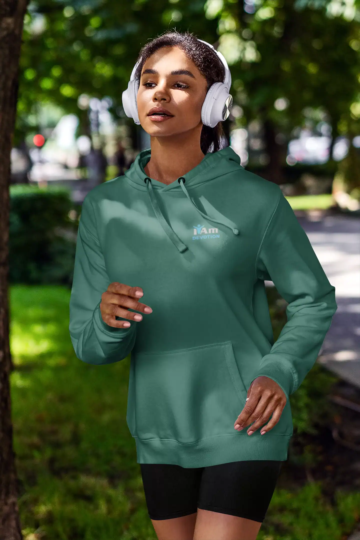 Young woman in green hoodie and headphones jogging outdoors.